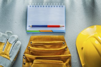 Protective gloves building helmet notebook pencil tool belt on concrete background