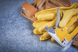 Composition of leather tool belt safety gloves stapler gun on metallic background construction