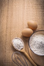 Vertical aerial view organized copyspace eggs flour in bowl spoon corolla on wooden board food and
