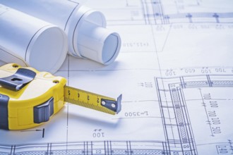 Close up view yello tapeline and rolls of blueprints horizontal version