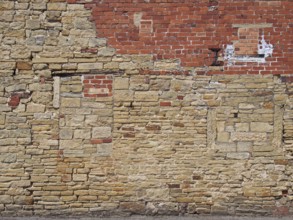 An old exterior wall with an irregular patched and repaired brick and stone surface