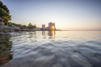 Castle ruins at dawn. Bay on the Mediterranean Sea with calm water at sunrise. Reflection of the