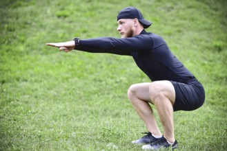 Full length of young concentrated sportsman doing squats outdoors