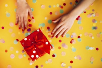 From above of anonymous female with wrapped present decorated with red ribbon and placed on yellow