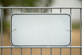 Unlabelled white sign on a fence with space for text