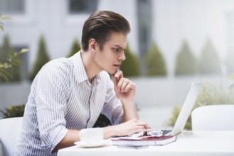 Smart attitude. Positive handsome man using a laptop and sitting in the cafe while surfing the