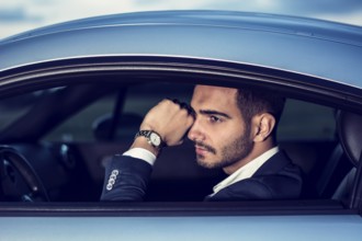 Portrait of young attractiave man in business suit sitting in his new stylish car outdoor in