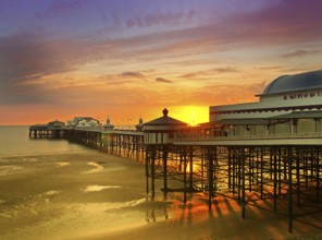 The sun setting over the historic north pier in blackpool with glowing golden light reflected on