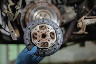 Clutch plate shown by a hand in blue glove in an automotive repair setting
