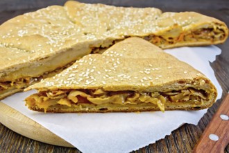 Pie with cabbage and sesame seeds with fresh rye dough knife on a wooden boards background