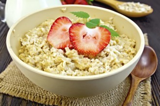 Oatmeal in a yellow cup with strawberries on a napkin of burlap, spoon, milk in a glass jar on the