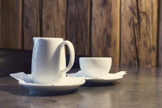 Cappuccino coffee with milk. Cup of cappuccino and jug of milk on wooden background