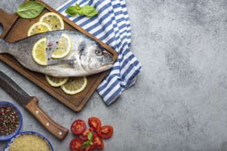 Raw fish dorado with ingredients lemon, fresh basil, cut cherry tomatoes, uncooked rice on wooden