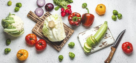 Fresh various vegetables with wooden cutting boards and knife on white kitchen table top view.