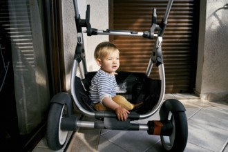 Little child sitting in a stroller on the balcony.