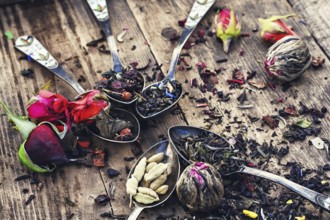 Varieties of tea brewed in an iron spoon on wooden background with buds of tea roses