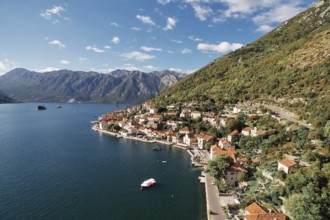 Boat is moored in the bay near the winding shore of Perast with a view of the bell tower.