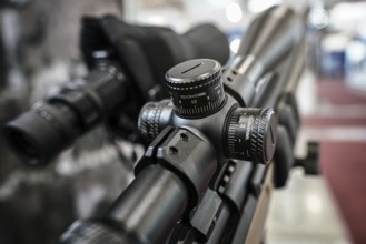 Black shooting scope optics mounted on rifle displayed at weapons exhibition fair, closeup detail