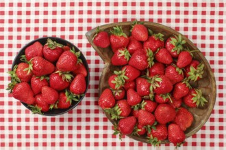 Top down view, strawberries in black and wooden carved bowl on red gingham pattern tablecloth,