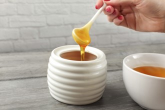 Detail on woman holding small ceramic spoon, filled with honey, about to put it in white tea cup
