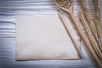 Bunch of wheat-rye ears wooden spoon corn pencil vintage paper on wood board