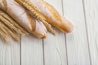 Two baguettes and ears of wheat on old white wooden boards with copyspace