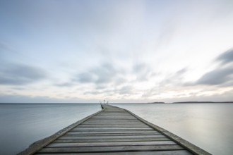 Sunrise over a lake in autumn. A wooden jetty juts into the water, while grass has established