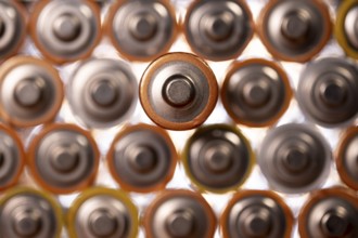 Multiple used AA alkaline batteries are seen arranged in a pile. Closeup front view from the plus