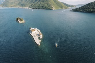 Motor boat sails on the sea past the island of Gospa od Skrpjela. Montenegro. Drone.