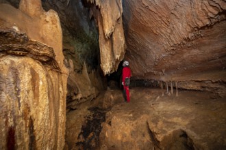 A speleologist with helmet and headlamp exploring a cave with rich stalactite and stalagmite