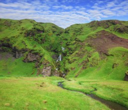 Basalt mountains covered in green moss and grass . Gorgeous cascading waterfall from melting