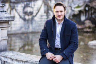 Photo of a man sitting by a serene pond on a stone wall