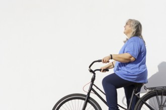 Smiling overweight mature woman riding a retro style bicycle isolated on white background and copy