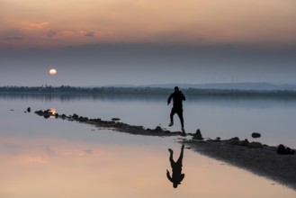 Unrecognised person running to reach the sun. Idyllic winter sunset at a lake. Silhouette