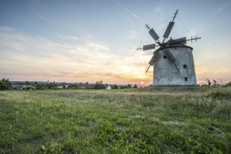 Windmill with wooden sails in a landscape with fields. Meadows and flowers appear in the sunset.