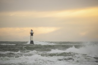 A lighthouse stands in the storm. Wild sea in the evening. Sunset on a coast with many rocks in the