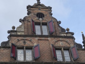 Historic brick façade with decorative elements and red shutters against a cloudy sky, nijmegen, the