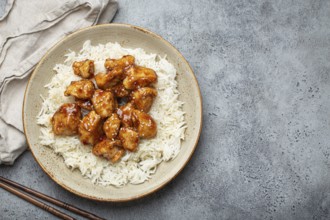 Chinese sweet and sour sticky chicken with sesame seeds and rice on ceramic plate with chopsticks