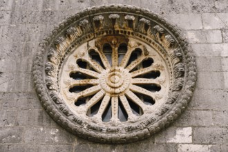 Rose window with ornaments and patterns on the dark stone wall of the church.