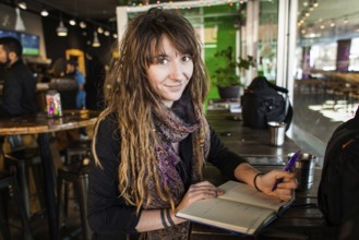 Portrait of smiling beautiful girl with dreadlocks and tattoos. Writing on a notebook with a pen in