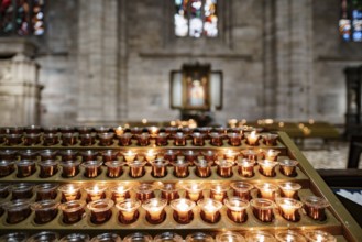 Votive candles are burning on a stand in the Duomo Cathedral. Close-up.
