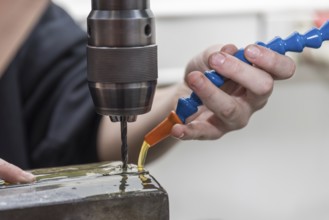 Skilled worker drills hole in steel with metal drill using cooling lubricant
