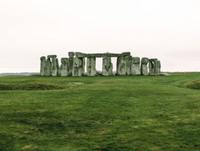 Warm-toned image of Stonehenge on a grassy field under a cloudy sky. Salisbury, England, United