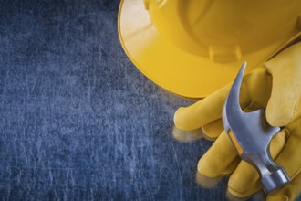 Pair of protective gloves hard hat and claw hammer on scratched metallic background construction