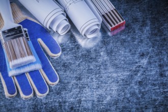 Wooden meter paint brush safety gloves blueprints on metallic background