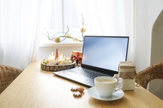 Laptop on a wooden desk by the window in an attic apartment. Gifts, advent candles, Christmas