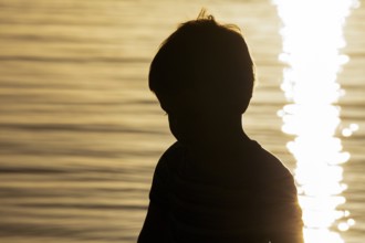 Silhouette of little boy by the sea at sunset