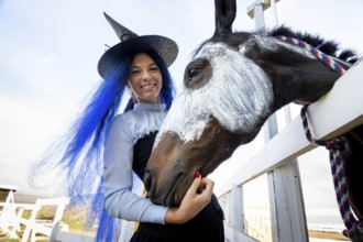 A girl dressed as a witch stands next to a horse on which a skeleton is drawn for the celebration
