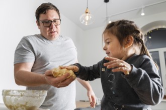 Father feeling playful with his caucasian little daughter, while preparing homemade dough for tasty
