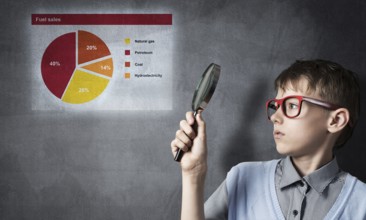 Cute boy looking through magnifying glass against graphs at chalkboard
